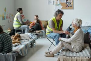Mature female volunteer in uniform holding hand of senior woman and comforting her while working in refugee camp